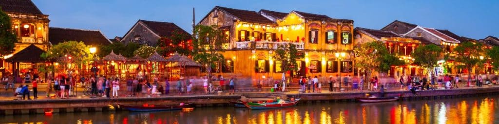 Hoi An Ancient Town at dusk with lit-up shops, colorful banners, and the Thu Bon River in the foreground