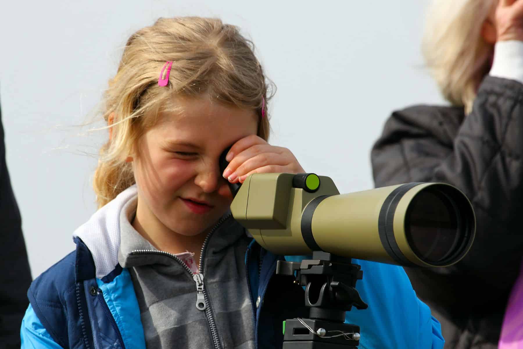 Young girl around 9 years old using a scope for birdwatching in nature