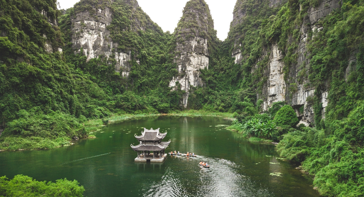Scenic landscape of Ninh Binh, Vietnam with emerald green waters, clear blue skies, and a traditional temple surrounded by lush nature