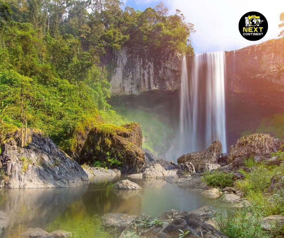The majestic K50 Waterfall cascades down a rocky cliff, surrounded by lush greenery in Kon Chu Rang Nature Reserve, Vietnam. Mist rises from the powerful flow, creating a serene yet dramatic landscape deep within the tropical forest.