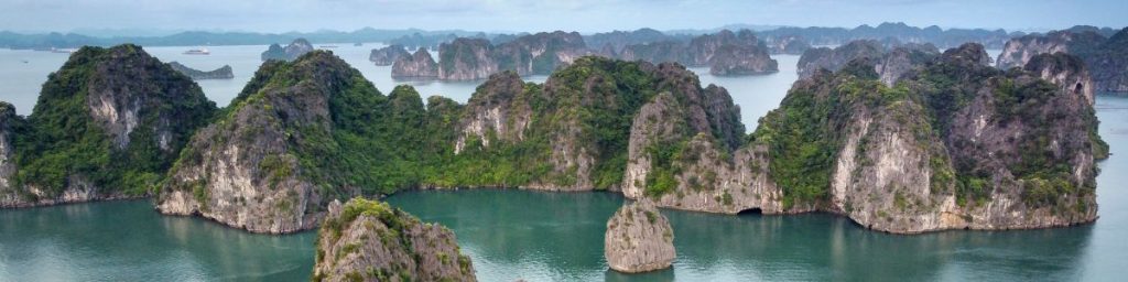 Aerial view of Ha Long Bay with limestone karsts, lush green vegetation, and calm blue waters under a clear sky