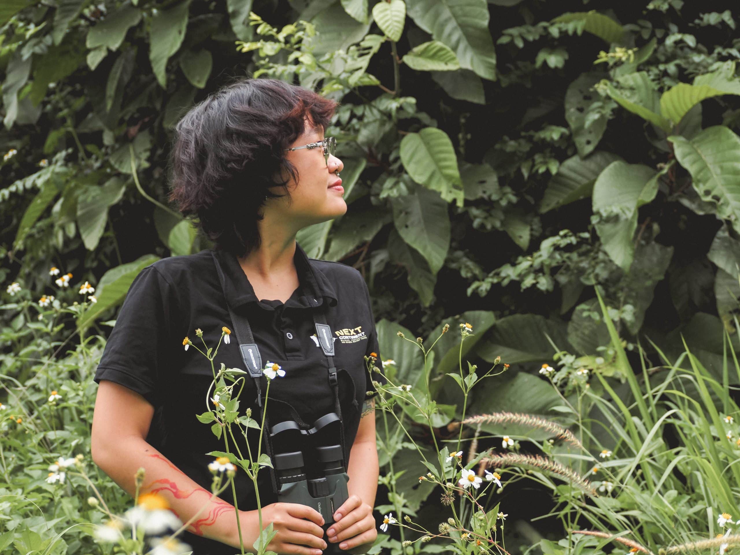 A girl in black, holding binocular, standing in the wild